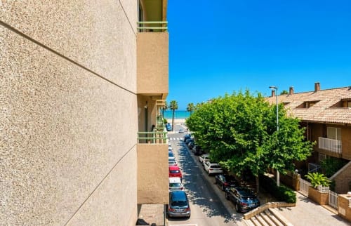Immeuble moderne à Valence avec vue sur rue, voitures garées, verdure luxuriante et accès à la mer à 50m