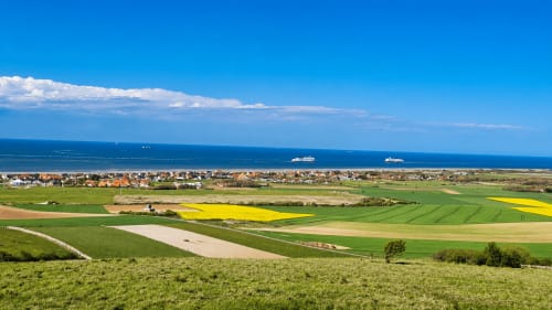Scenic coastal view of Sangatte countryside with green fields, yellow rapeseed crops, and sea horizon near Ô de Mer