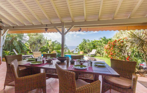 Terrasse de la Villa  avec table à manger, chaises en rotin, jardin tropical et vue mer sur la piscine et la mer des Caraibes.