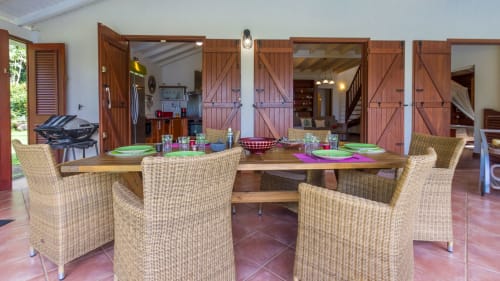 Terrasse de la Villa  avec table à manger, chaises en rotin, vue sur la cuisine et le salon/TV.