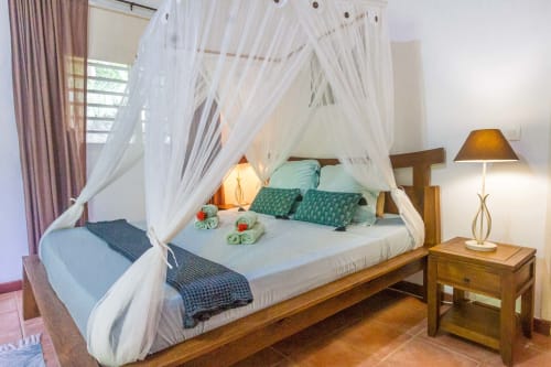 Grande chambre climatisée avec lit 160, moustiquaire et armoire de rangement. Vue sur le jardin tropical.
