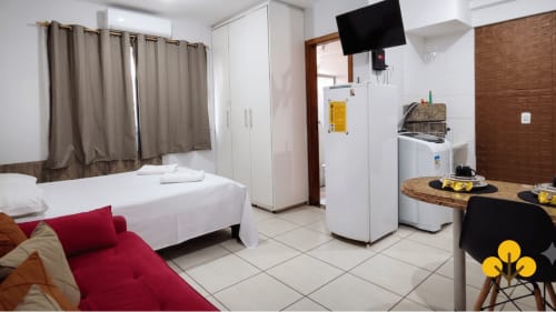 Kitnet em Wellington Rodovalho, Goiânia, com cama, sofá vermelho, kitchenette, máquina de lavar e TV de tela plana