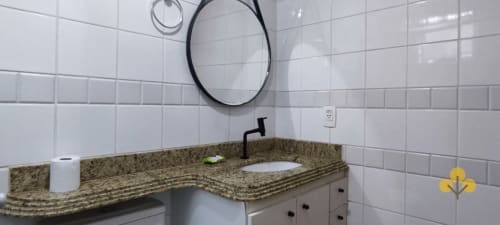 Pia de banheiro moderna com bancada em granito, torneira preta e espelho redondo no apartamento-hotel Wellington Rodovalho