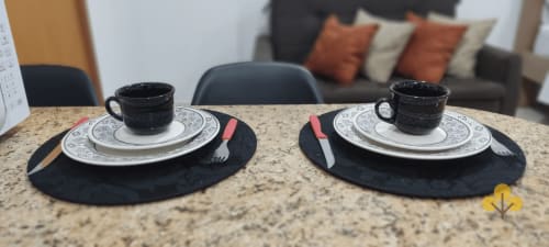 Dois talheres com xícaras pretas e pratos decorativos sobre marcadores escuros no flat Wellington Rodovalho em Goiânia