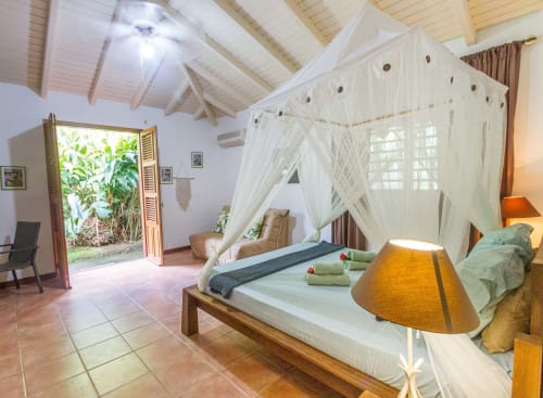 Grande chambre climatisée avec lit 160, moustiquaire et armoire de rangement. Vue sur le jardin tropical.