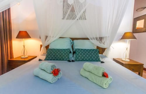 Grande chambre climatisée avec lit 160, moustiquaire et armoire de rangement. Vue sur le jardin tropical.