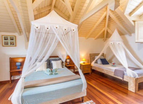 Chambre luxueuse avec lits à baldaquin blancs, poutres en bois apparent et vue sur mer aux Villas Amboise Guadeloupe