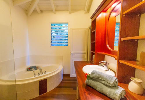 Salle de bain luxueuse à la Villa Jasmine, Villas Amboise Guadeloupe avec baignoire arrondie, meuble vasque en bois et miroir rouge