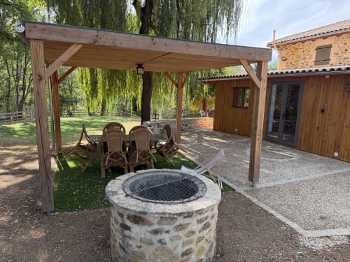 Pergola en bois avec foyer en pierre et assises au jardin de réception du Domaine de Brise Bois à Rouzède