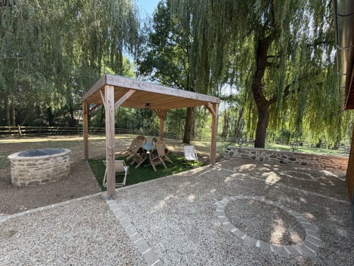 Pergola en bois avec coin détente au jardin du Domaine de Brise Bois, Rouzède, entouré de saules pleureurs et d'un foyer