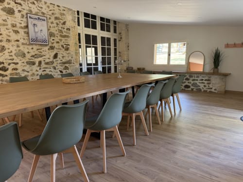 Salle à manger contemporaine du Domaine de Brise Bois avec table en bois massif, chaises vert sage et murs en pierre rustique à Rouzède