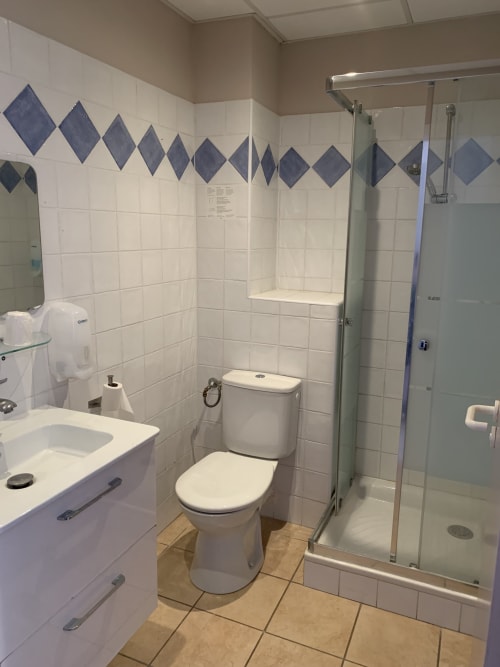 Salle de bain moderne de l'hôtel Le Clos du Thoronet avec carrelage blanc, toilettes, lavabo et douche vitrée à Le Thoronet