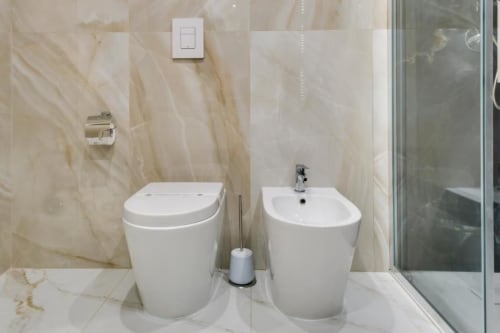 Bagno moderno dell'hotel Domus Praeclara Merulana con pareti in marmo, bidet e WC bianchi, e doccia in vetro