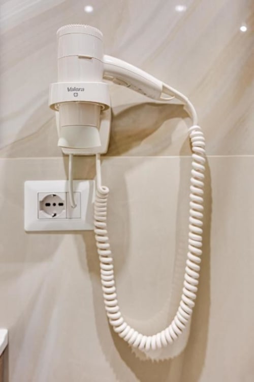 Valeara wall-mounted hair dryer in beige bathroom with coiled cord and electrical outlet, Domus Praeclara Merulana hotel