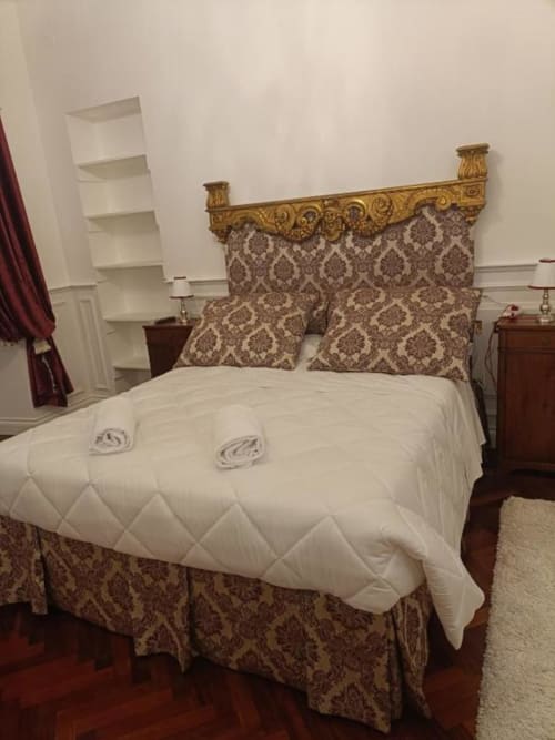 Camera Magna Mater con testata dorata ornamentale, cuscini damascati, trapunta trapuntata bianca e comodini in legno