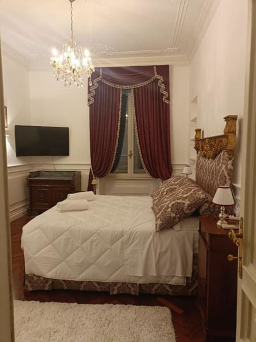Camera da letto elegante nella suite Magna Mater con letto a quattro colonne, drappeggi bordeaux, lampadario di cristallo e stile classico