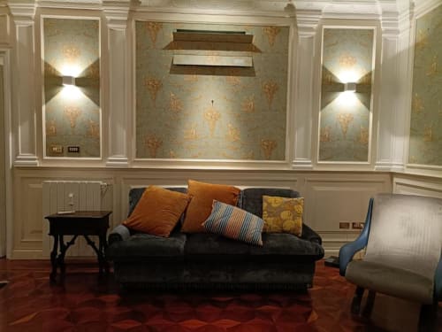 Soggiorno della suite Magna Mater con divano scuro, cuscini arancioni, carta da parati ornamentale e elegante arredamento da hotel italiano