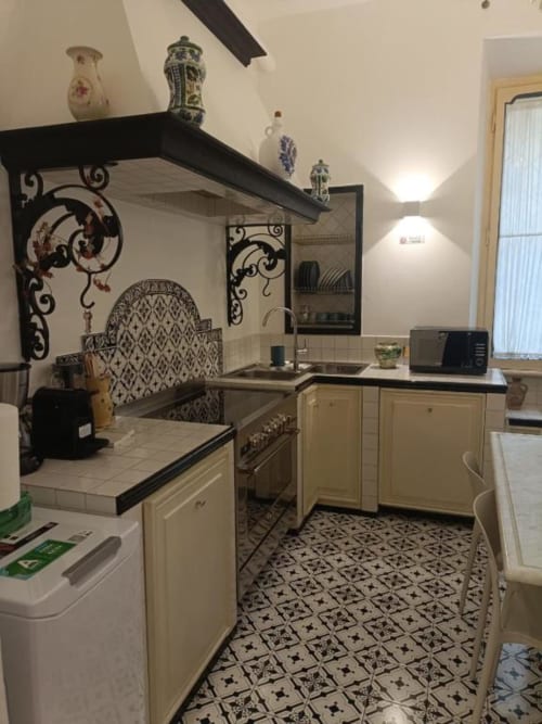 Cucina Magna Mater con mobili color crema, ripiani neri ornamentali, piatti decorativi, piastrelle decorate e design moderno
