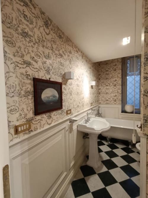 Elegante bagno della Magna Mater Suite con carta da parati toile ornamentale, lavandino a colonna, pavimento bianco e nero a scacchi e quadri