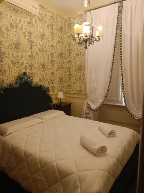 Camera elegante nella Suite Magna Mater con carte da parati ornate, testata nera, biancheria bianca e tende drappeggi