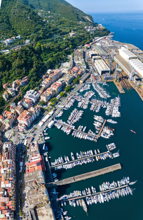 Vista aerea della marina di Castellammare di Stabia con barche, edifici sul lungomare e collina boscosa