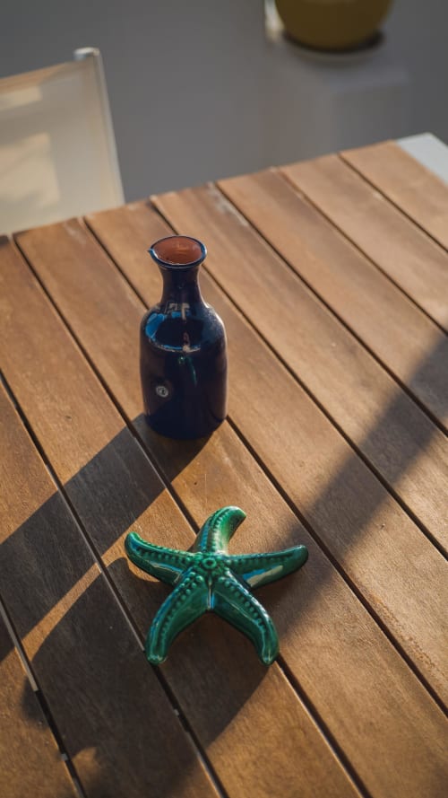 Bottiglia di vetro blu scuro e stella marina in ceramica verde su tavolo in legno all'hotel Fraledune di Campomarino di Maruggio
