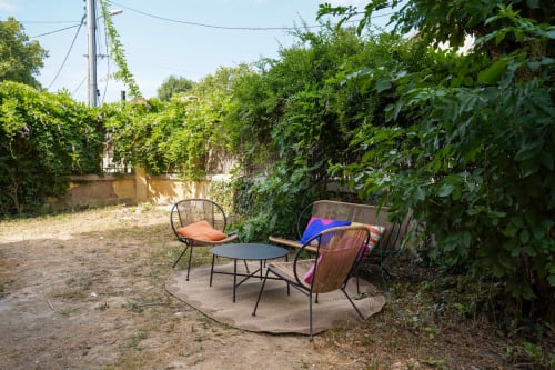 Coin salon confortable au Le 1 Péraudel avec table ronde, chaises rembourrées et verdure luxuriante à Castres