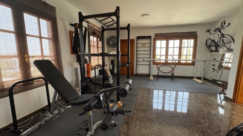 Modern home gym at Villa Estrella Polar in Tahiche with weight bench, black frame machine, bicycle rack, and large windows