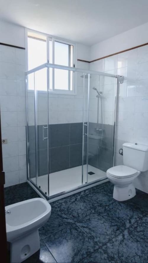 Baño moderno con ducha de cristal, inodoro blanco y suelo de azulejos oscuros en Apartamentos Jucar, Frontera