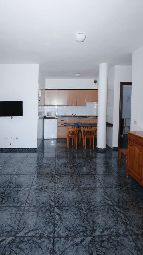 Moderna cocina y sala de estar con piso de mármol oscuro, sillas de comedor de madera y gabinetes blancos en Apartamentos