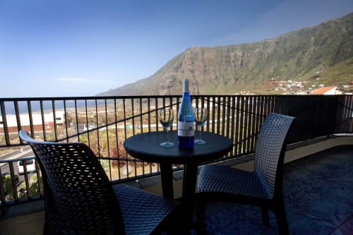 Balcón con vistas al mar en Apartamentos Jucar, Frontera, con mesa, sillas, botella de vino y vistas a montañas costeras