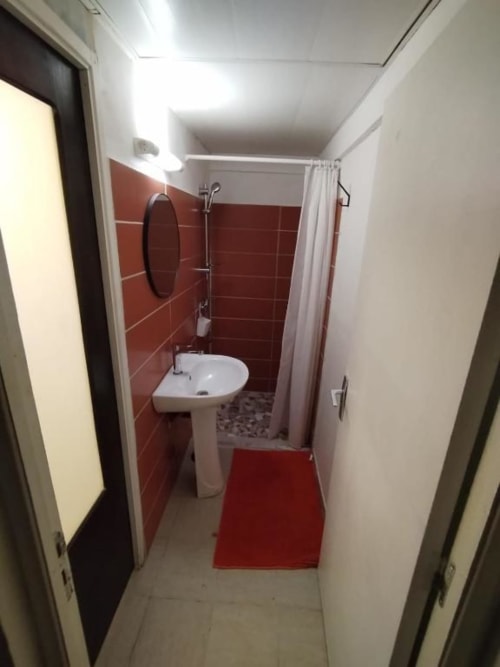 Salle de bain moderne à l'auberge Sunshine Conciergerie, Fort-de-France : lavabo sur colonne, carrelage rouge et douche dans chambre 1 lit