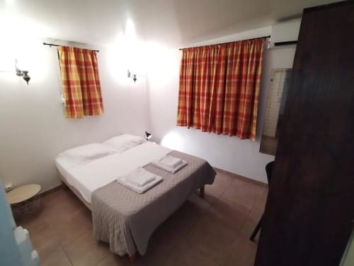 Chambre au gîte Sunshine Conciergerie à Fort-de-France avec lit double, rideaux rouges et vue sur la cour intérieure.