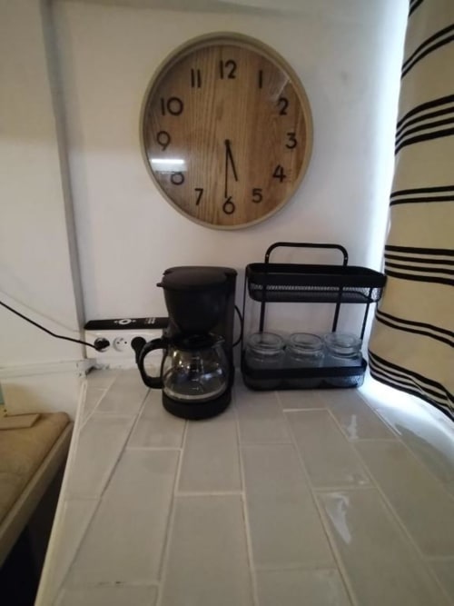 Coin cuisine de l'appartement Sunshine Conciergerie avec cafetière, micro-ondes, horloge murale et rideau à rayures