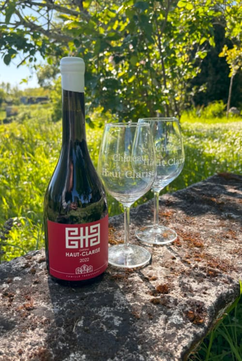 Bouteille de vin Château Haut Clarise et verres dans le jardin du vignoble de Belvès-de-Castillon