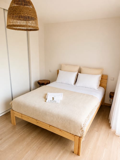 Quarto moderno nos Terra Clara Studios com cama de madeira, roupas de cama brancas, luminária de palha tecida e decoração em tons creme em Esposende,