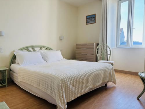 Chambre double lumineuse à l'Hôtel Du Rocher au Caylar avec tête de lit verte, literie blanche, parquet et vue sur la ville