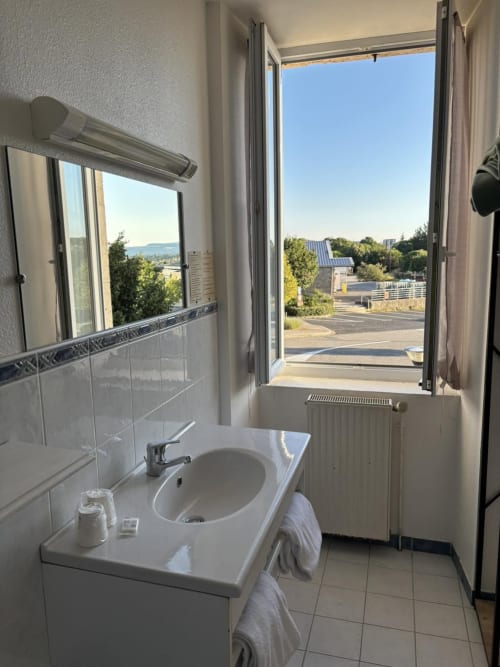 Helles Badezimmer im Hôtel Du Rocher mit Stadtblick durch offene Türen mit Blick auf Le Caylar