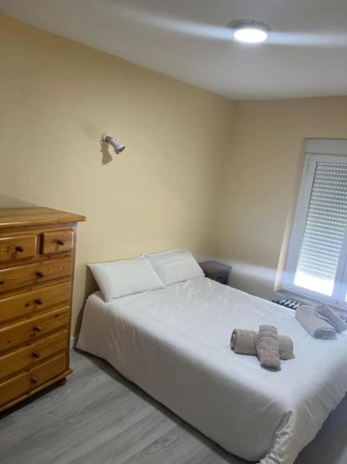 Dormitorio doble limpio en Hostal Restaurante El Encuentro en Barraco con cama blanca, cómoda de madera y ventana con persianas