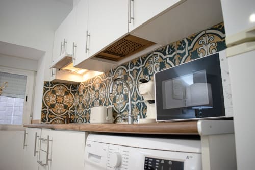 Cocina moderna con gabinetes blancos, azulejos de backsplash azules y dorados ornamentados, microondas y encimera de madera en Mérida