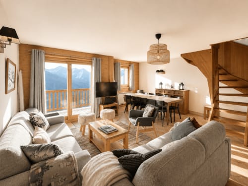 Spacious mountain apartment living room with snow-capped Alps view, wooden beams, comfortable seating, fireplace, and modern