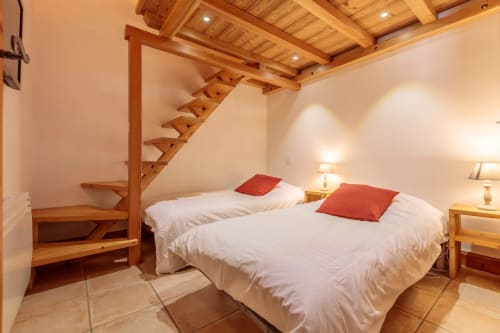 Chambre de montagne moderne avec deux lits, oreillers rouges, escalier mezzanine en bois et éclairage contemporain