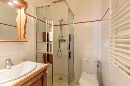 Salle de bains moderne avec douche walk-in, carrelage blanc, accents rouges, meuble vasque en bois, sèche-serviettes, toilettes à Arc 1800