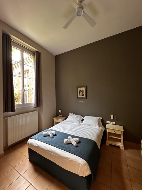 Cottage bedroom at La Recreation in Missillac with double bed, ceiling fan, and large window overlooking historic 1850 school