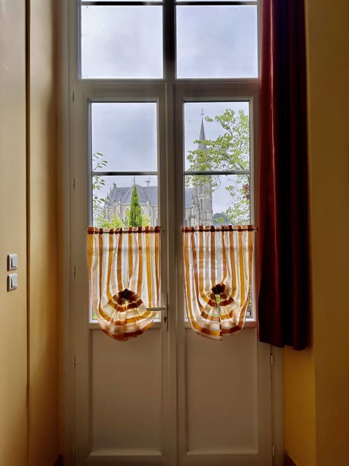 Cottage window view of Missillac church tower, striped cafe curtains, historic 1850 school building