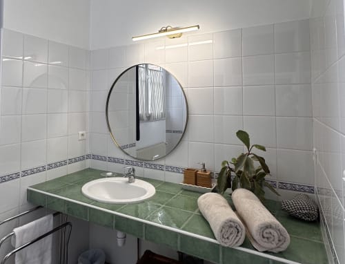 Modern bathroom in La Recreation cottage with green tile vanity, round mirror, and white towels in Missillac