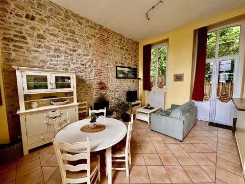 Bright cottage living area in historic 1850 schoolhouse with exposed brick, dining table, and French doors in Missillac