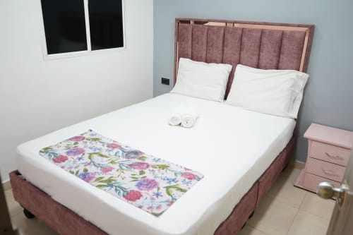 Habitación con cama doble en Casa Mango Cali, cabecero rosa, sábanas blancas y manta floral