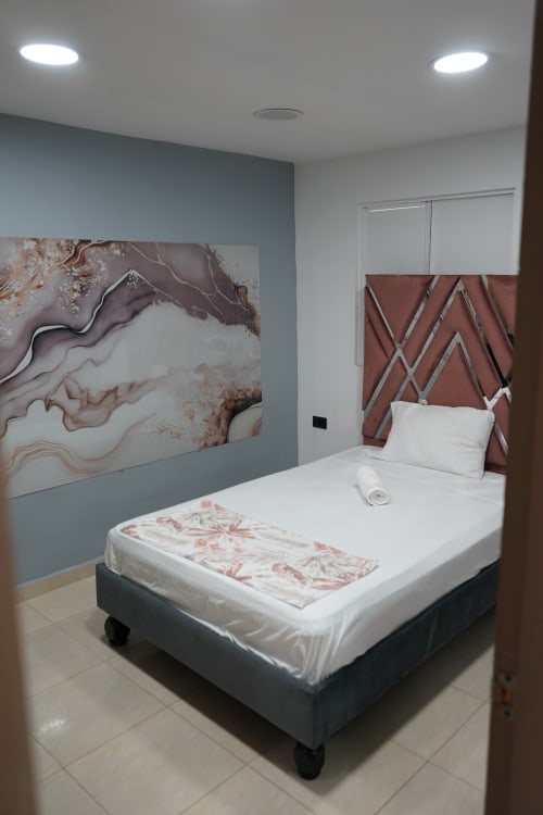 Habitación moderna del hotel CASA MANGO en Cali con cama de cabecera geométrica, arte mural abstracto e iluminación contemporánea.