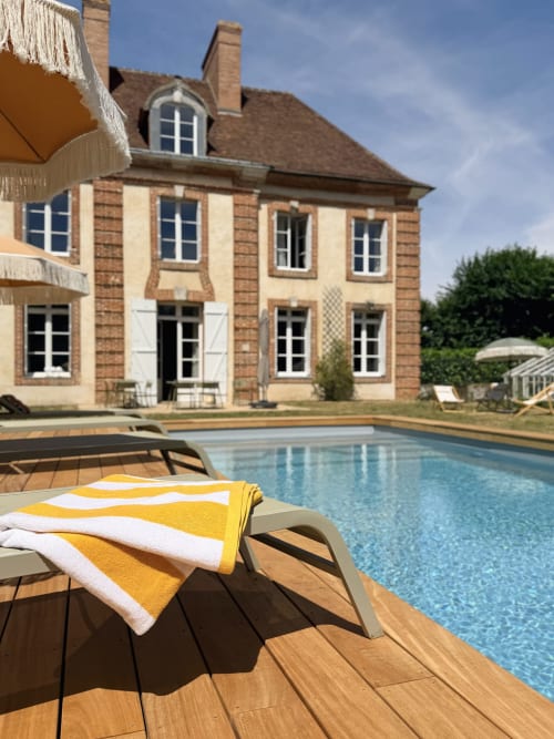 Maison Mansel B&B au bord de la piscine avec transat jaune, manoir normand et piscine bleue